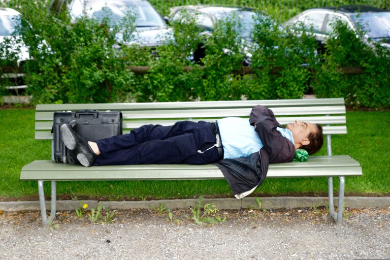 Tired person sleeping on a park bench during the day, illustrating what it can feel like to wake up tired after sleep.