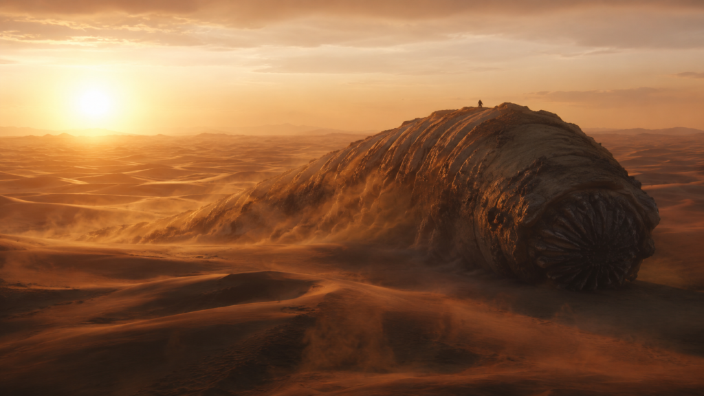 A distant rider crosses a massive sandworm-like creature in an alien desert at sunset. From Dune: Part Three