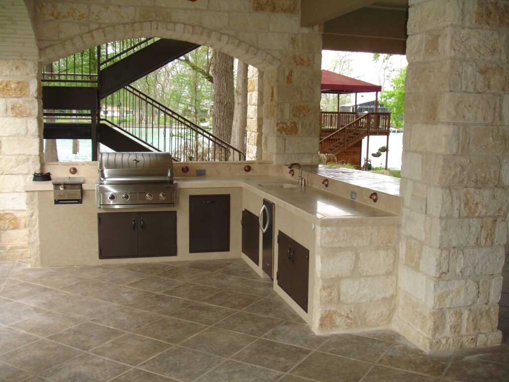 Built-in stone outdoor kitchen with grill, sink and covered patio structure.